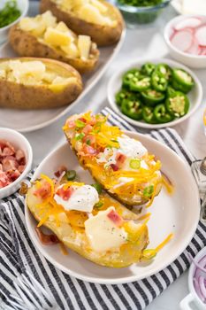 Pressure Cooker Baked Potatoes. Garnished large baked potatoes with butter, sour cream, cheese, and bacon bits on a white plate.