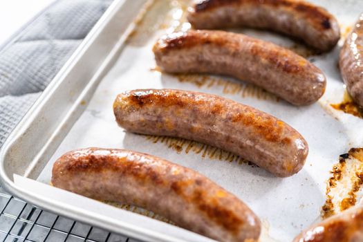Freshly cooked in oven beer bratwursts on a baking sheet lined with parchment paper.
