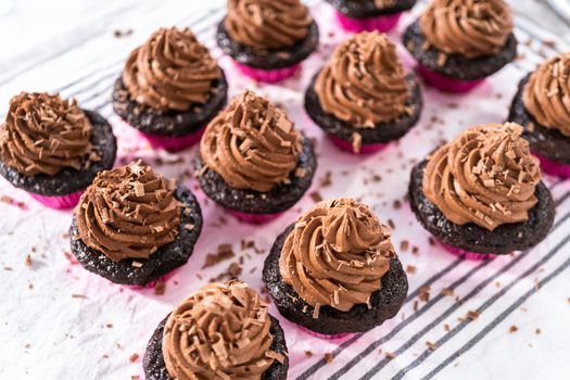 Piping chocolate ganache frosting on top of chocolate cupcakes.