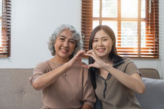 Loving adult daughter hugging older mother on couch at home, family enjoying tender moment together, young woman and mature mum or grandmother looking at each other, two generations.