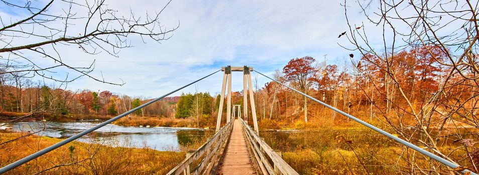 Image of Panorama of long suspension bridge going over Michigan river with fall foliage colors