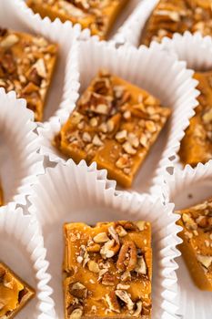 Homemade pumpkin spice fudge square pieces in white paper cupcake liners on a kitchen counter.