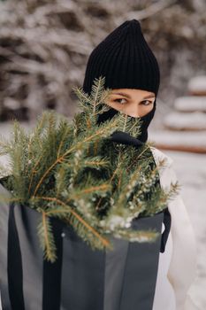 A girl in a white suit and balaclava with a package of Christmas trees in the winter forest on New Year's Eve.New Year's concept.