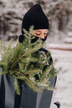 A girl in a white suit and balaclava with a package of Christmas trees in the winter forest on New Year's Eve.New Year's concept.