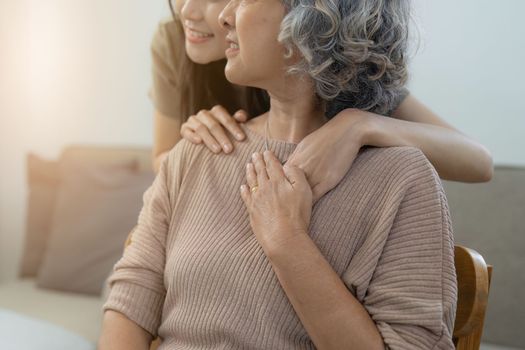 Loving adult daughter hugging older mother on couch at home, family enjoying tender moment together, young woman and mature mum or grandmother looking at each other, two generations.