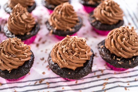 Piping chocolate ganache frosting on top of chocolate cupcakes.