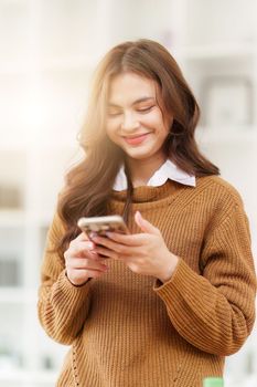 Young Asian Woman using smart phone at home. Female holding cellphone checking email or social media on internet.