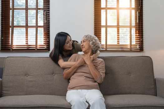 Loving adult daughter hugging older mother on couch at home, family enjoying tender moment together, young woman and mature mum or grandmother looking at each other, two generations.