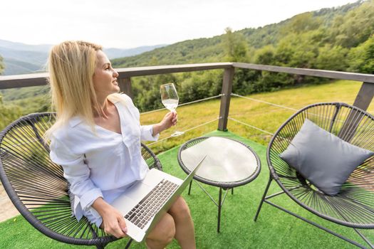 Successful positive business woman is sitting on an outdoor terrace with a notebook in a sun lounger. Remote work with laptop in the fresh air and freelance, people lifestyle, freedom concept.