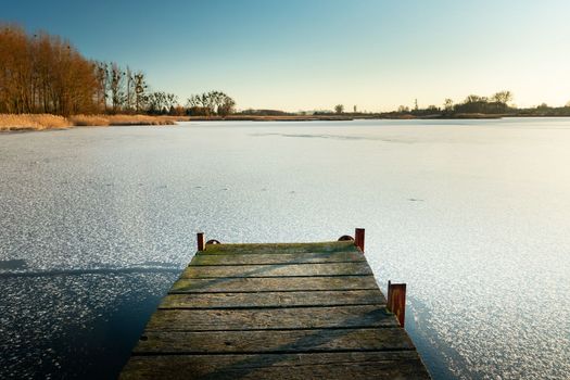 Wooden pier towards the frozen lake, winter landscape in Stankow, Poland