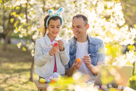 father and daughter coloring easter eggs with laptop.