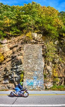 Image of Motorcycle driving on road from side past cliffs and stone wall patch with blue graffiti