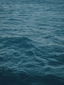 Vertical view of dark blue-green color of water surface with waves in middle of endless deep sea. Dark blue waves in deep ocean. Raging aquamarine waves on surface of the water