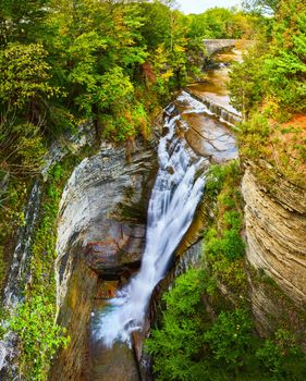 Image of Stunning large waterfall into deep gorge with stone bridge in background