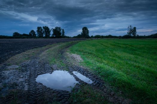 Puddle on the rural road through the fields and cloudy evening sky, September in the eastern Poland