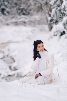 Portrait of a stylish woman in a white suit with elegant gloves sitting in nature in winter.
