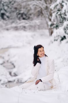 Portrait of a stylish woman in a white suit with elegant gloves sitting in nature in winter.