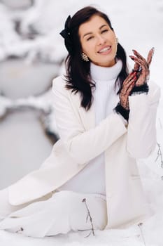 Portrait of a stylish woman in a white suit with elegant gloves sitting in nature in winter.