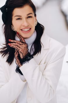 Portrait of a stylish woman in a white suit with elegant gloves sitting in nature in winter.