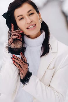 Portrait of a stylish woman in a white suit with elegant gloves sitting in nature in winter.