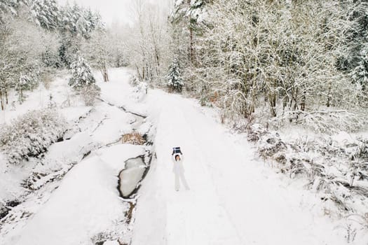 A stylish woman with a white suit with a New Year's gift in her hands in a winter forest. A girl in nature in a snowy forest with a gift box.