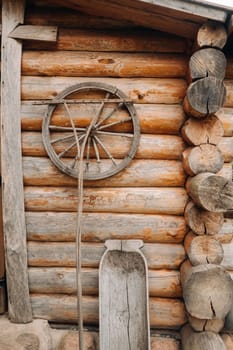 An old wooden wall of a house in the village and ancient cart wheels, tools, etc.
