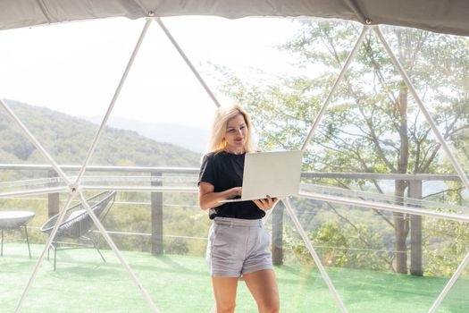 Young caucasian woman using and watching on laptop computer on in dome camping hotel. Tourism, vacation and weekend