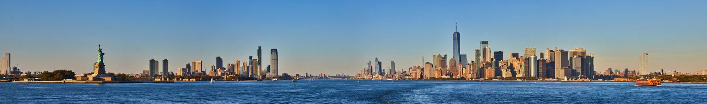 Image of Wide panoramic view of southern Manhattan New York City and New Jersey with Statue of Liberty from waters near sunset