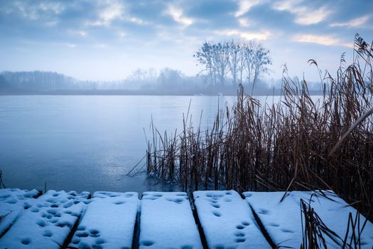 A snow-covered pier and a frozen, misty lake, winter nature landscape