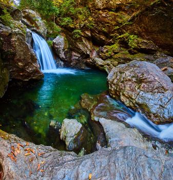 Image of Wide view of rocks surrounded peaceful pool of water with waterfall in cliffs