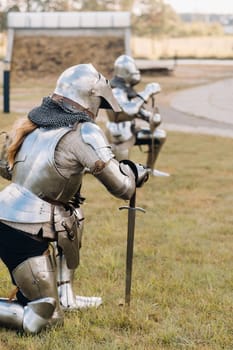 two knights in ancient metal armor stand at the stone wall of the castle.