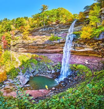 Image of Stunning vibrant forest and cliffs with large waterfall pouring over rocks down below to turquoise waters