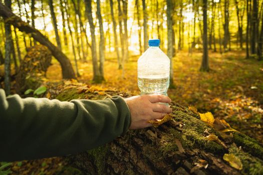 Male hand with a bottle of water, view in the autumn forest, October sunny day