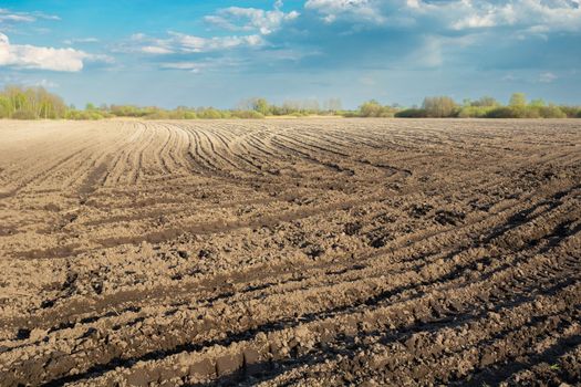 Soil in a plowed farmland, wheel marks on the field, spring rural view