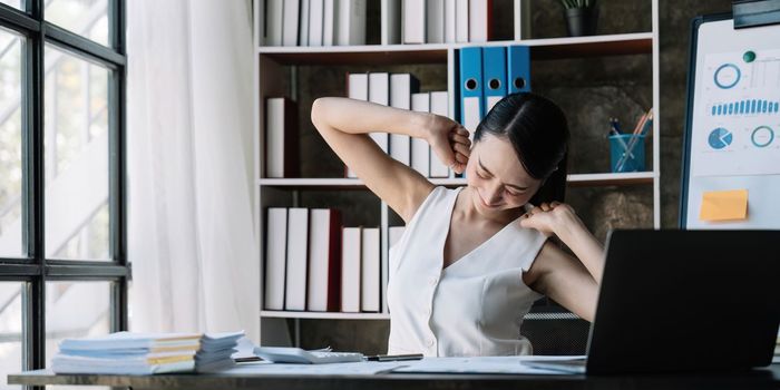 Businesswoman or working lady is stretch themselves or lazily for relaxing on their desk while doing their work in the office.