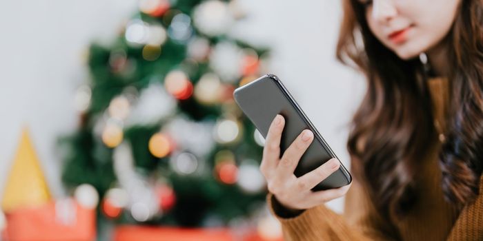 Close up hand of woman using her Mobile Phone at home. Boke christmas tree background.