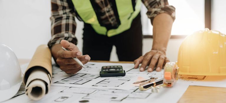 Close up of civil male engineer asian working on blueprint architectural project at construction site at desk in office