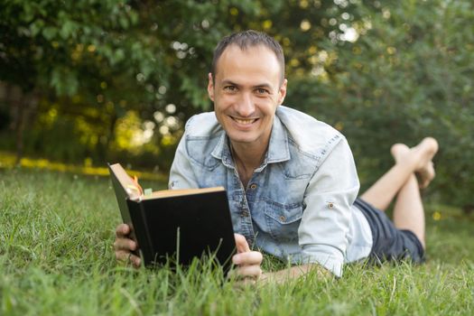 Young man lying in the grass, relaxing and reading a book.