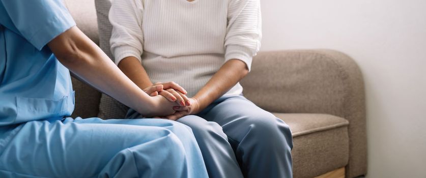 Happy patient is holding caregiver for a hand while spending time together. Elderly woman in nursing home and nurse.