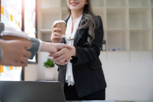 Two Asian businesswomen are shaking hands in the office. business cooperation, business dealing, Congratulations, greeting. close-up hands image.