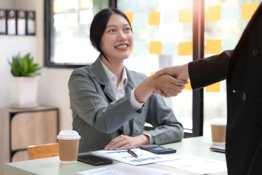 Two Asian businesswomen are shaking hands in the office. business cooperation, business dealing, Congratulations, greeting. close-up hands image.