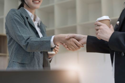 Two Asian businesswomen are shaking hands in the office. business cooperation, business dealing, Congratulations, greeting. close-up hands image.