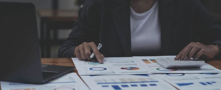 Businesswoman press the white calculator to calculate the numbers in the company financial documents, the finance department prepares the document and forwards it to be checked before the meeting..