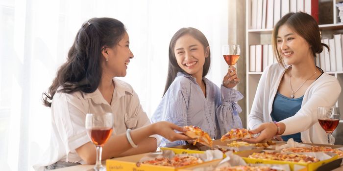 Group of Asian friends gather to celebrate Christmas with champagne and eating pizza at home. Joy of holiday party with friends or colleague concept.