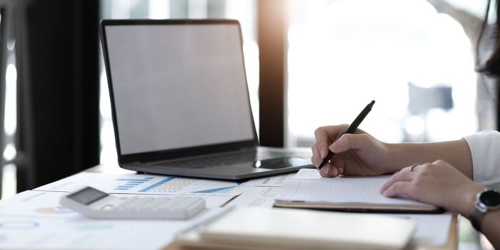 Young business woman sitting at table and taking notes in notebook.On table is laptop, smartphone.