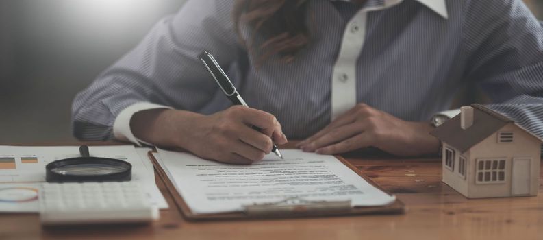 Looking for real estate agency, property insurance, mortgage loan or new house. Woman with magnifying glass over a wooden house at her office.