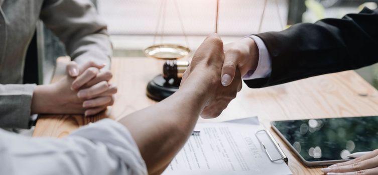 Close up of woman lawyer hand and man client shaking hand collaborate on working agreements with contract documents at the office..