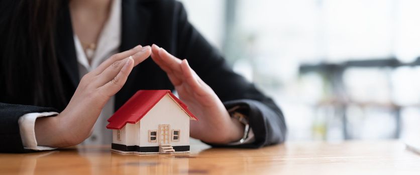 Wooden toy house protected by hands with copy space. Home insurance concept. banner ratio.