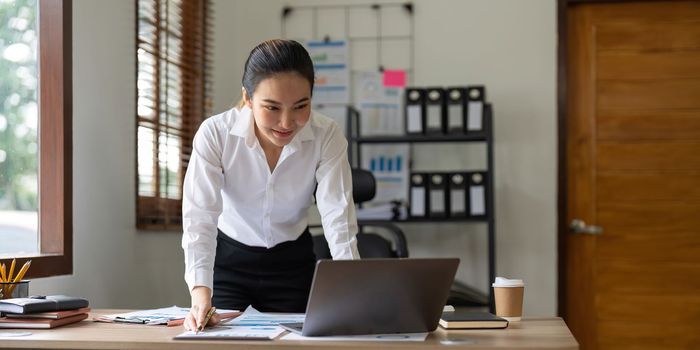 Beautiful Asian Businesswoman using on laptop for financial analysis