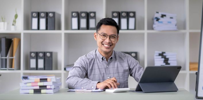 Portrait of joyful excited Asian guy using pc sitting at desk looking at laptop screen, raising hands with excitement, ecstatic enthusiastic